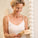 Smiling woman in a white top holding a Tropic Skincare gift box while standing in front of a bathroom mirror.